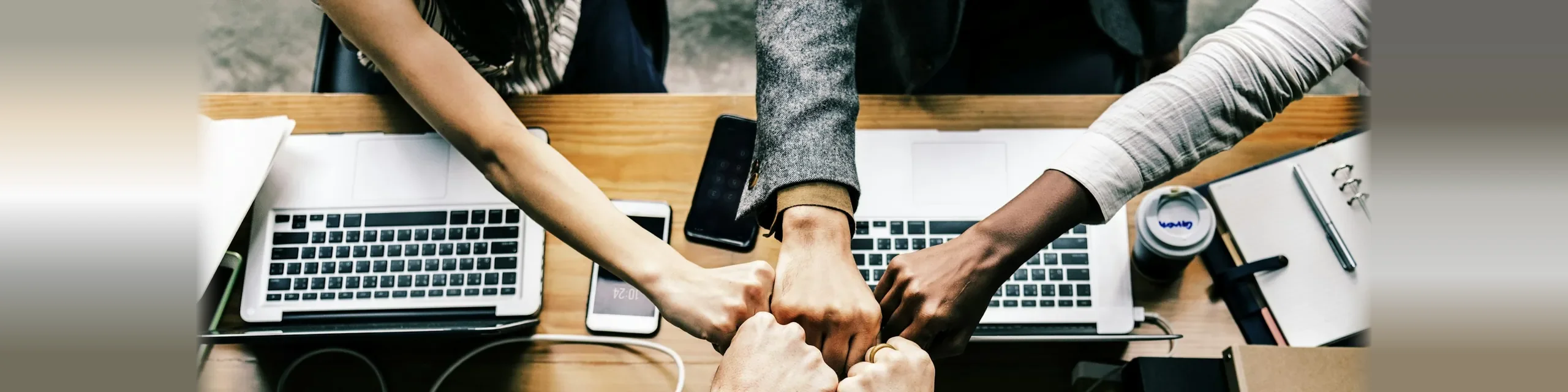 Startup team bumping fists over laptops at a shared desk