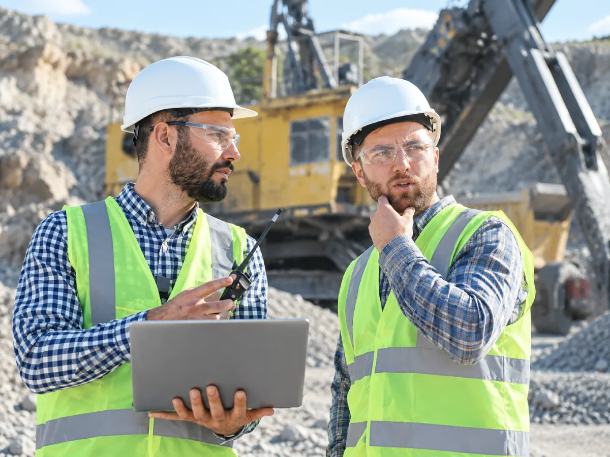 Two colleagues in safety gear reviewing data on a tablet